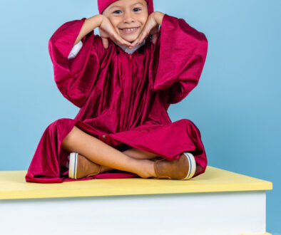 Niño con toga y birrete sobre escenario de libros durante sesión de graduación escolar en Costa Rica