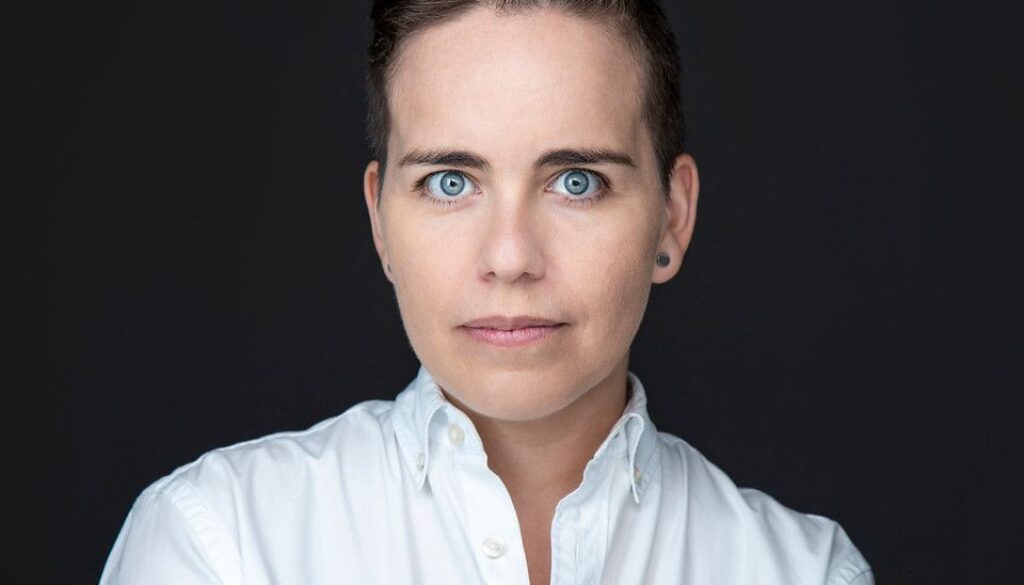 Fotografía corporativa de Ana Mora con camisa blanca sobre fondo negro.