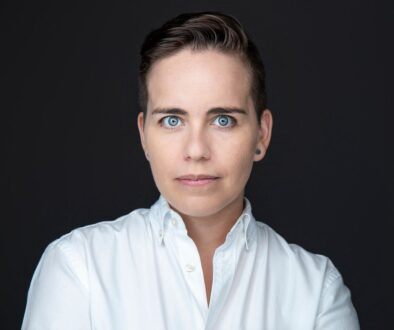 Fotografía corporativa de Ana Mora con camisa blanca sobre fondo negro.
